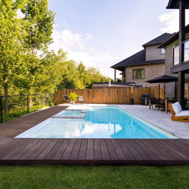 A sleek rectangular fiberglass pool in “Sydney Harbour” style with Arctic Shimmer finish, surrounded by stone decking and reflecting a clear sky.