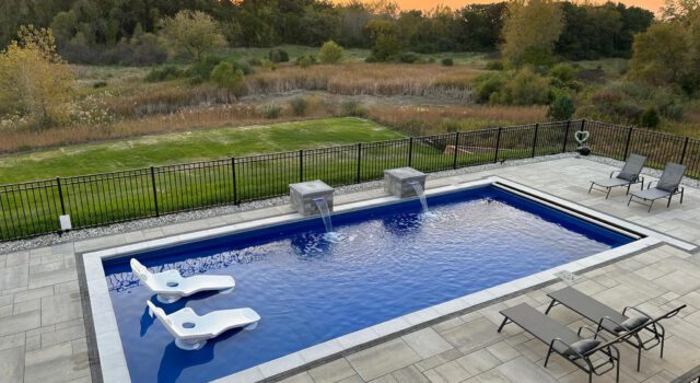 A long, rectangular fiberglass pool with a shallow sun ledge, featuring a shimmering blue water color.